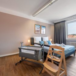 Babybett, Hochstuhl und Kinderschutzgitter im sandfarbenen Einzelschlafzimmer.
