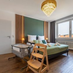 Babybett, Hochstuhl und Kinderschutzgitter im grünen Einzelschlafzimmer.